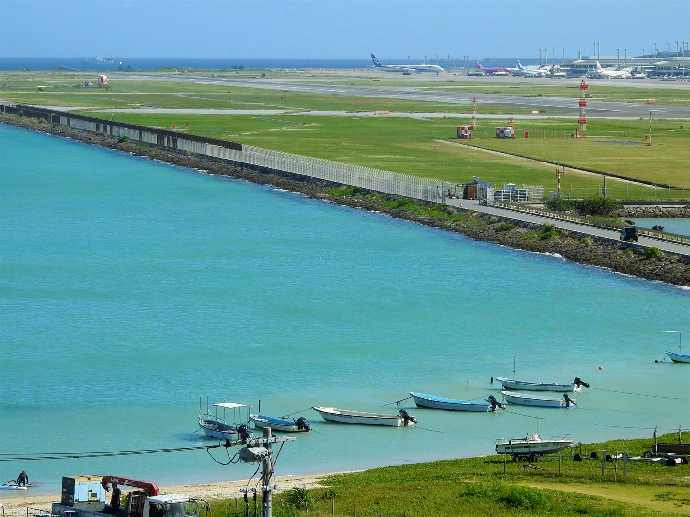 瀬長ビーチと那覇空港の方向を望む景色。手前に海と小さな船、奥に滑走路が見える